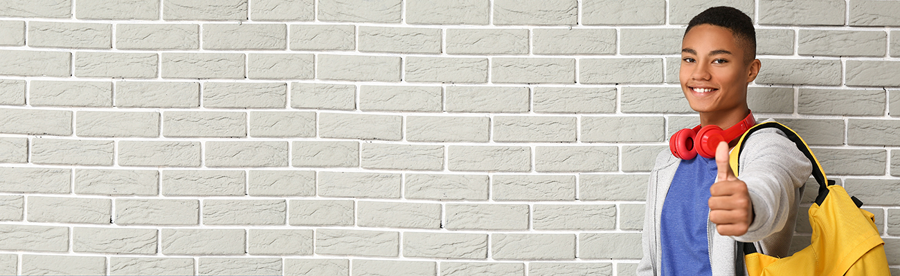 teenager-secondary-male-student-thumbs-up-grey-brick-wall