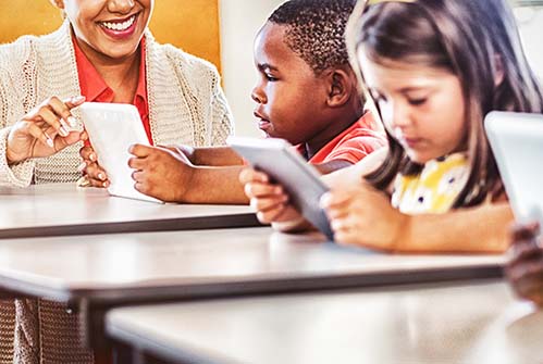 teacher-with-elementary-students-at-desk-using-tablets