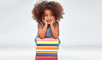 T-reading-elementary-girl-smiling-with-pile-of-books-on-grey-background.jpg